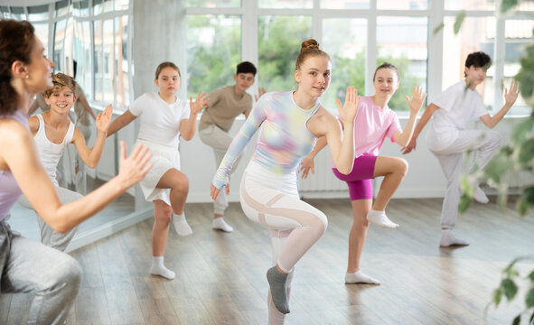 Girl teen performs modern dances repeats movements of unrecognizable teacher together with friends during lesson at choreographic school. Hobbies, active pastime