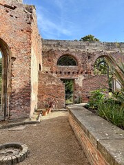 Obraz premium Historic brick ruins with arched windows and open courtyard, blending weathered architecture, textured masonry, and greenery under a bright blue sky in natural daylight.
