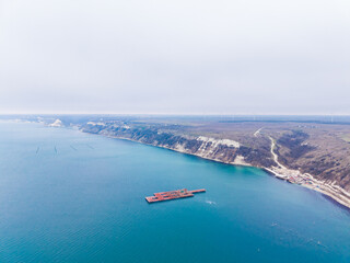 Obraz premium Cement platform in the sea with coastline view near wind turbines and cliffs on an overcast day