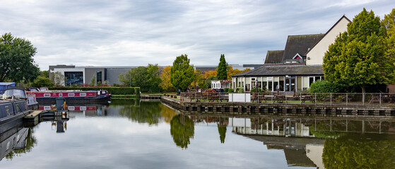 Tranquil Canalside Village Scene With Boats, Cafes, And Reflections On Still Water