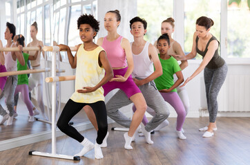 Adult female trainer helps group of teenage dancers perform plie movement correctly