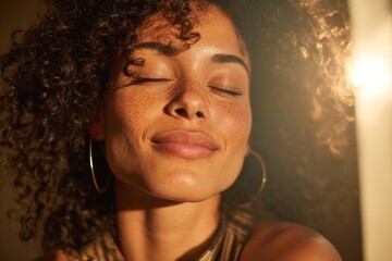 A woman smiles softly with closed eyes as warm light touches her freckled face and curly hair creating a calm close up portrait
