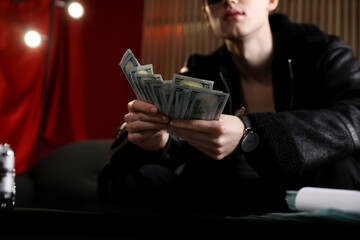 Young businessman in jacket with dollar banknotes on sofa indoors, closeup