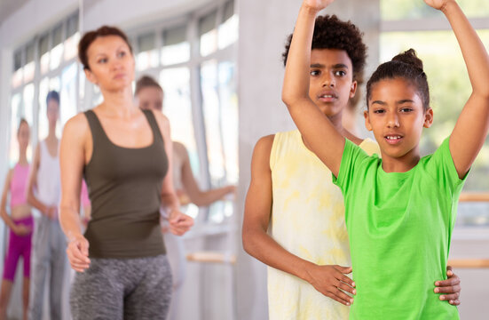Thin teenage girl practicing ballet positions in pair with boy in dancehall during dancing classes