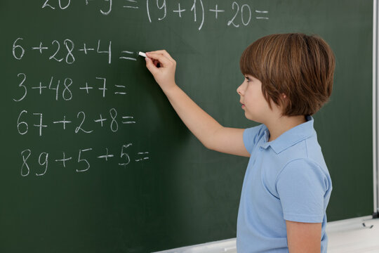 Schoolboy doing math on chalkboard in classroom