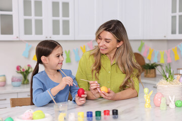 Naklejka premium Easter celebration. Mother and her daughter painting eggs at white marble table in kitchen