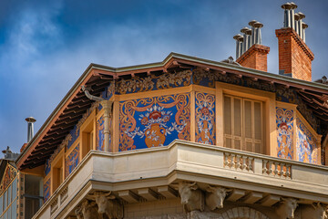 Ornate Belle Epoque building with blue and gold floral Sgraffito frescoes and stone bull head sculptures supporting a grand balcony in Nice, France © SvetlanaSF