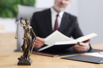 Notary in suit reading book at wooden table in office, focus on statue of Lady Justice