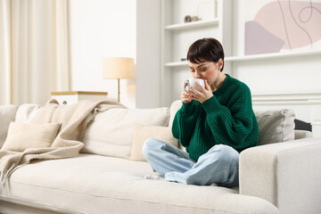 Fototapeta premium Woman having tasty hot drink on sofa at home. Space for text