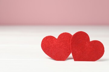 Obraz premium Love. Red decorative hearts on white table against pink background, closeup. Space for text