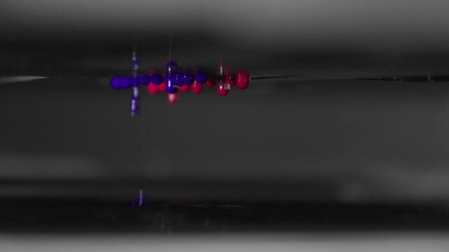 4K macro footage of red and blue ink drops falling from a UV printer's print head. Close-up of the modern printing process and technology.