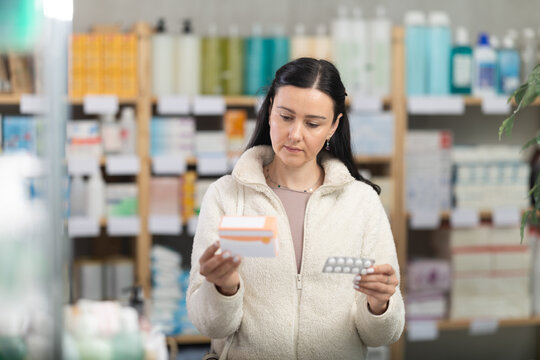 European woman chooses a pack of pills standing in a bird near the counter with medical goods and drugs. Customer chooses migraine pills