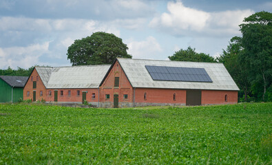 Obraz premium Large brick barn building with rooftop solar panels by green field.