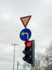 Traffic signals at an intersection showing a red light and a left turn yield sign near a city street during the day