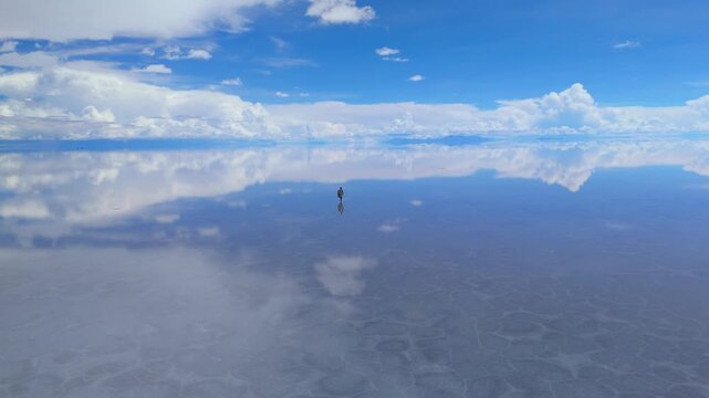 A solitary figure traverses the expansive Salar de Uyuni salt flats in Bolivia, under a clear blue sky