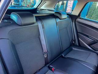 Car interior shows backseat space with black fabric and cushions while parked in a residential area during daylight