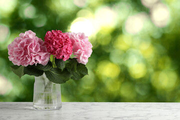Bouquet of beautiful hydrangea flowers in glass vase on table against blurred green background,...