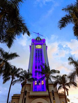 Sunset view of Aloha Tower in Hawaii with palm trees and colorful lights glowing