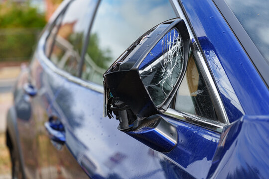 Broken side mirror with shattered glass on a blue car after an accident or collision