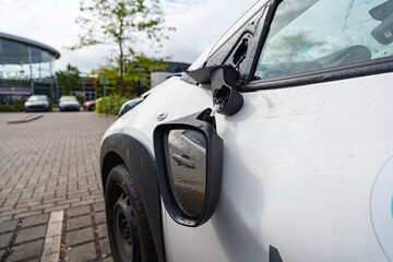 Broken side mirror on white city car after collision, showing clear impact damage