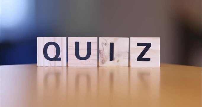 Wooden blocks spelling the word QUIZ arranged in a row on a reflective surface.