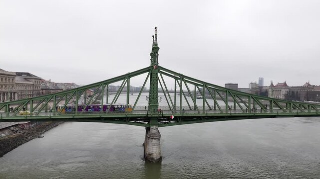 Aerial moves forward across the Danube River toward the iconic green ironwork of the Liberty Bridge (Szabads&aacute;g h&iacute;d) in Budapest, Hungary, on an overcast day