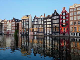 Obraz premium Historic Damrak Waterfront with Iconic Dancing Houses Reflecting in Amsterdam Canal