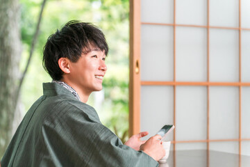 Obraz premium A man in a yukata looking at his smartphone in a Japanese-style room at a ryokan