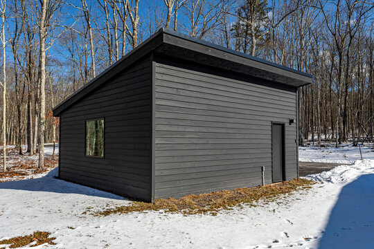 Modern minimalist outbuilding with slanted roof in winter forest setting