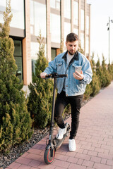 Young and handsome man with electric scooter using smartphone standing against the background of office buildings. Using gadgets in work and everyday life.