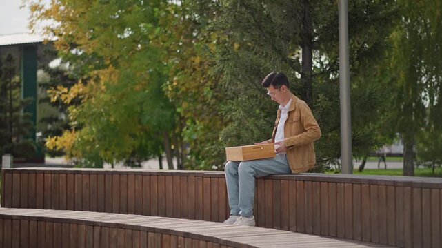 young man sketching on park bench, casual jacket and jeans, autumn trees and scattered leaves, focused on wooden drawing board, quiet urban green space, soft sunlight, contemplative mood, street art