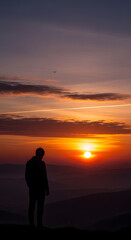 Fototapeta premium Man Silhouette Contemplating Dramatic Sunset Over Mountain Landscape