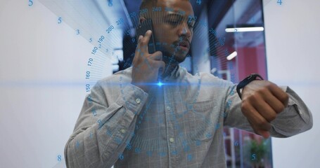 Holding phone to ear, worker wearing gray checked shirt checking watch in office corridor with HUD