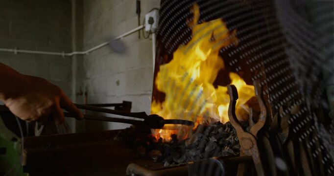 Metalworker heating metal in coal fire with tongs, sparking as grill casting dot shadows across arm