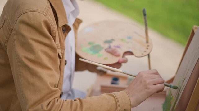 closeup artist brushwork on canvas, focused study of strokes and texture with steady hand, hands mixing vibrant green on palette, portable easel setup on park bench, workshop demo and technique