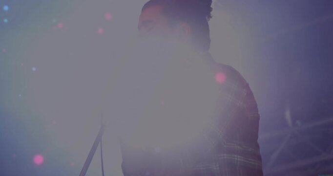 Male singer gripping vintage mic and performing song on music stage backlight flaring into shadow