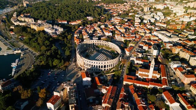 Cinematic 4K aerial orbit of the Pula Arena amphitheater. Ancient Roman stone architecture and historic cityscape at sunset in Croatia.