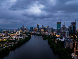Austin, Texas skyline shining on the waters of Colorado River, creating a breathtaking view as night falls under a dramatic, cloud filled sky
