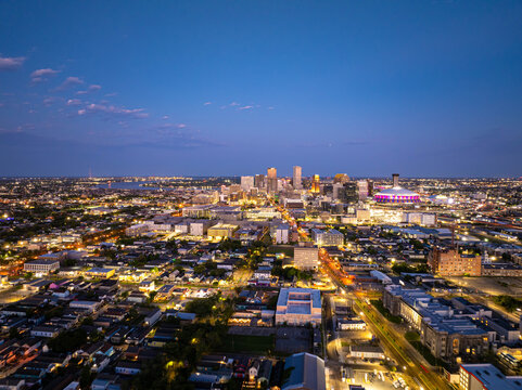 Aerial view of New Orleans skyline illuminating at dusk, showcasing vibrant city lights, prominent buildings, and the iconic Caesar Superdome under a beautiful twilight sky