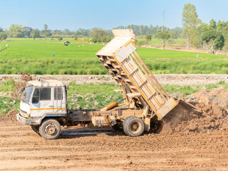 Tipper truck unloading and dumping a brown soil at land reclamation and ground leveling.