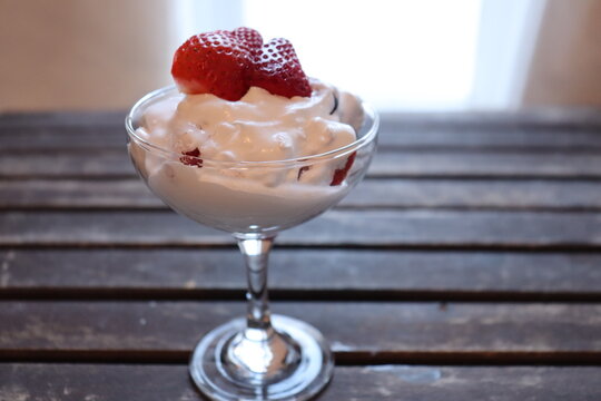 Berry dessert with whipped cream or yaourt and in a coupe glass. Creamy dessert in a transparent glass and on a wood background. Delicious fruit snack with creamy texture.