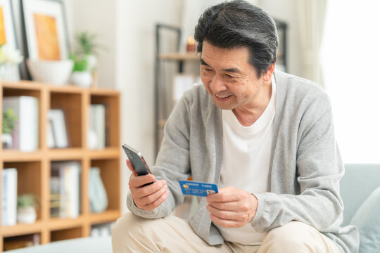 リビングでクレジットカートとスマホを見るミドルの男性