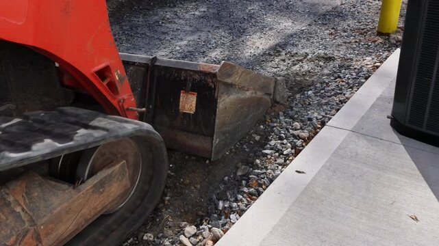 Tractor machine with bucket moves gravel at construction site as workers prepare for road repairs.