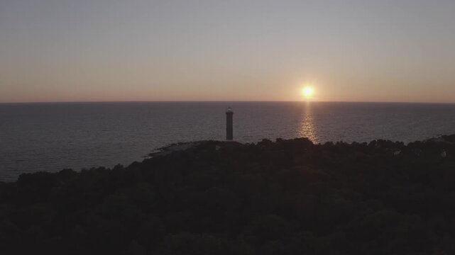 Scenic aerial view of a coastal lighthouse on Dugi Otok, Croatia, backlit by the setting sun and surrounded by open sea.