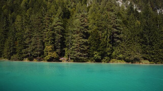 Drone panning along turquoise Weissensee shoreline with pine forest and mountains
