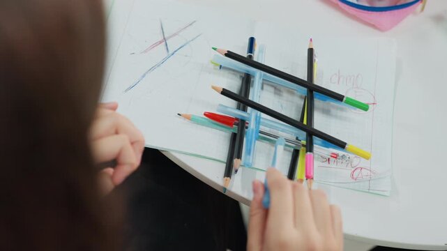 student hands arranging colored pencils on notebook creating playful grid during study break, closeup of fingers moving pens and markers, visible doodle marks and sketch lines, soft natural light,