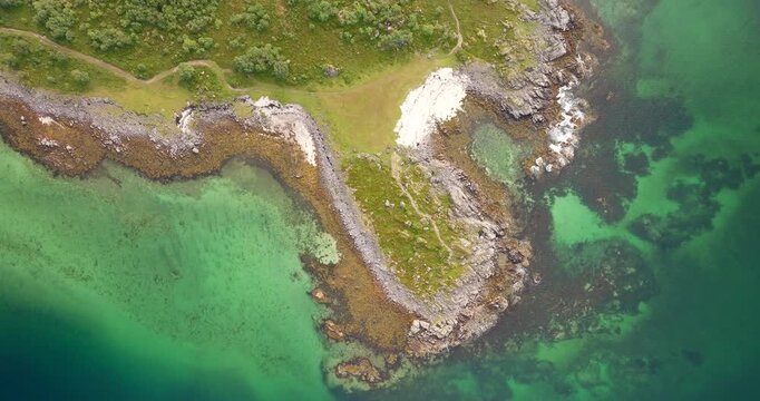 Aarnessan coastline near Stokmarknes shows rocky shorelines meeting clear turquoise water and green landforms, top down aerial