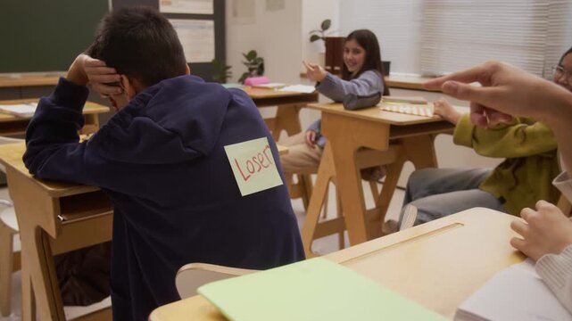 Close up shot of young boy sticking LOSER note on back teasing and making fun of classmate in school