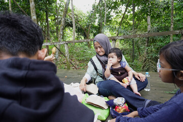 Asian Muslim mother having a picnic lunch with her son and daughter in the middle of the forest, family bonding