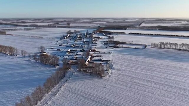 Cinematic horizontal aerial shot flying forward toward a small rural village in China. The houses are nestled in the center of vast, pristine white snow-covered land. Perfect for winter travel and hom